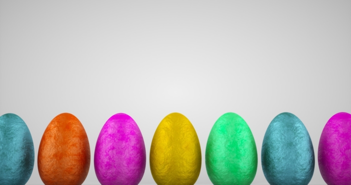 A row of standing assorted coloured foil chocolate eggs against a grey background