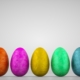 A row of standing assorted coloured foil chocolate eggs against a grey background