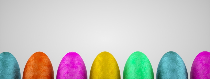 A row of standing assorted coloured foil chocolate eggs against a grey background